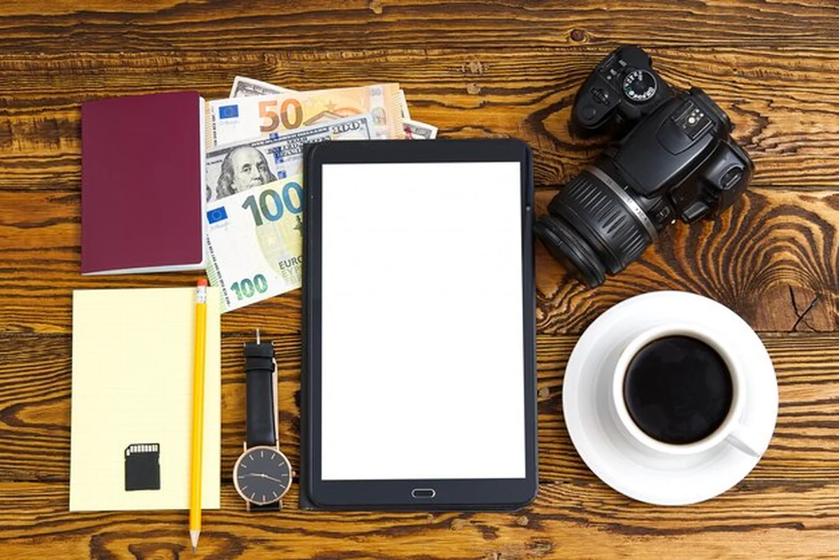 Przedmioty podróżne na drewnianym stole: paszport, aparat, pieniądze, tablet, kawa