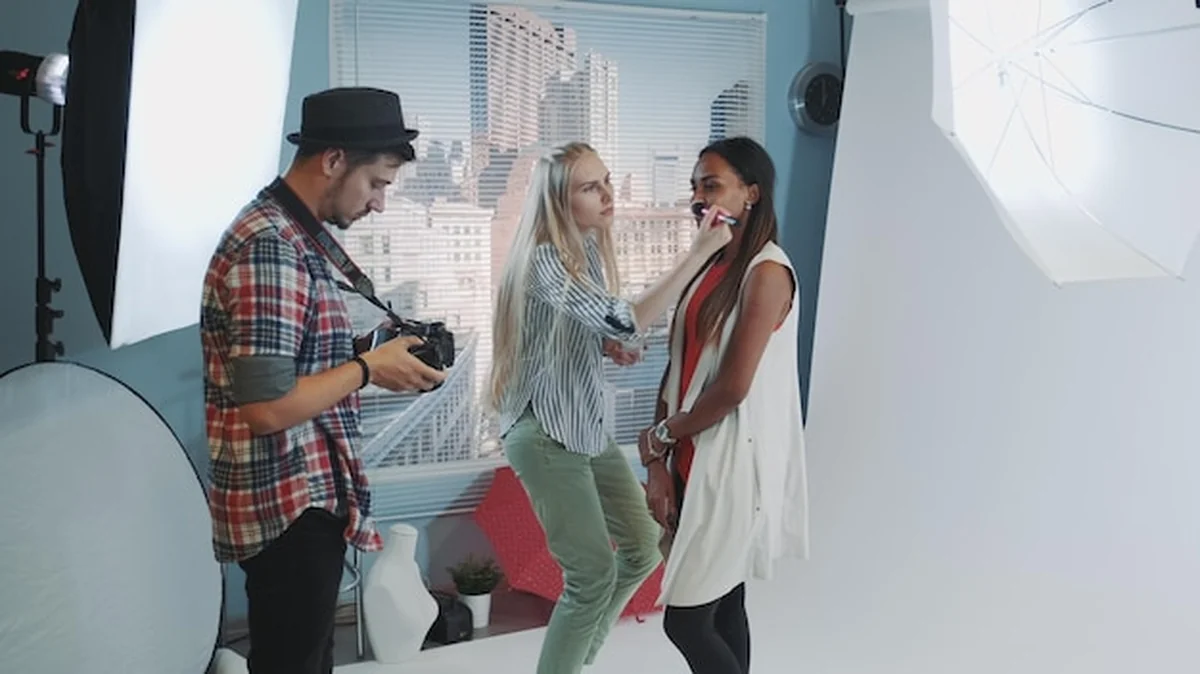 Fotograf stojący z kobietą nakładającą makijaż na model w studiu