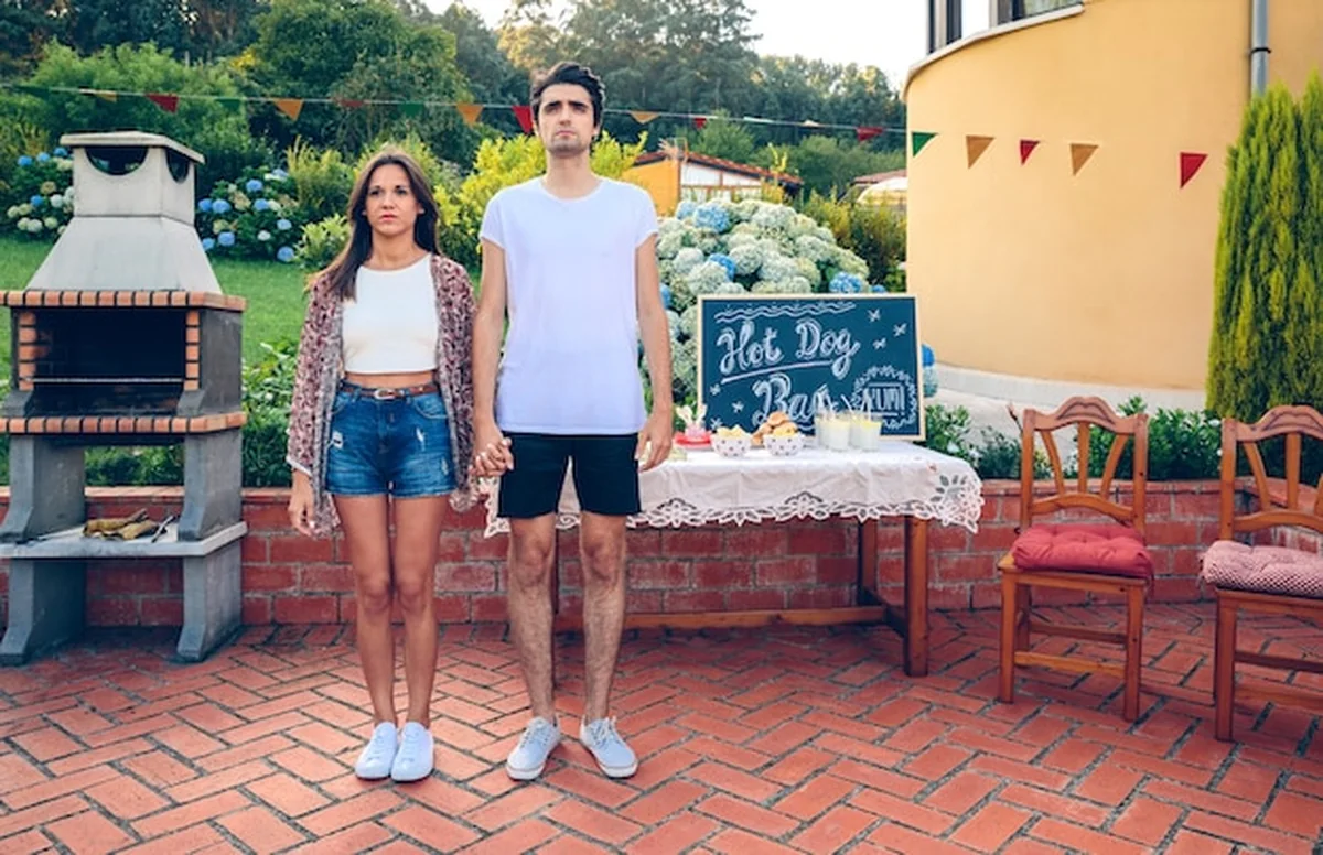 Młoda para przed grillem i stołem z jedzeniem na letniej imprezie na świeżym powietrzu